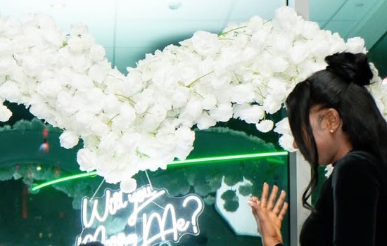 Proposal moment under a white floral arch with a neon sign